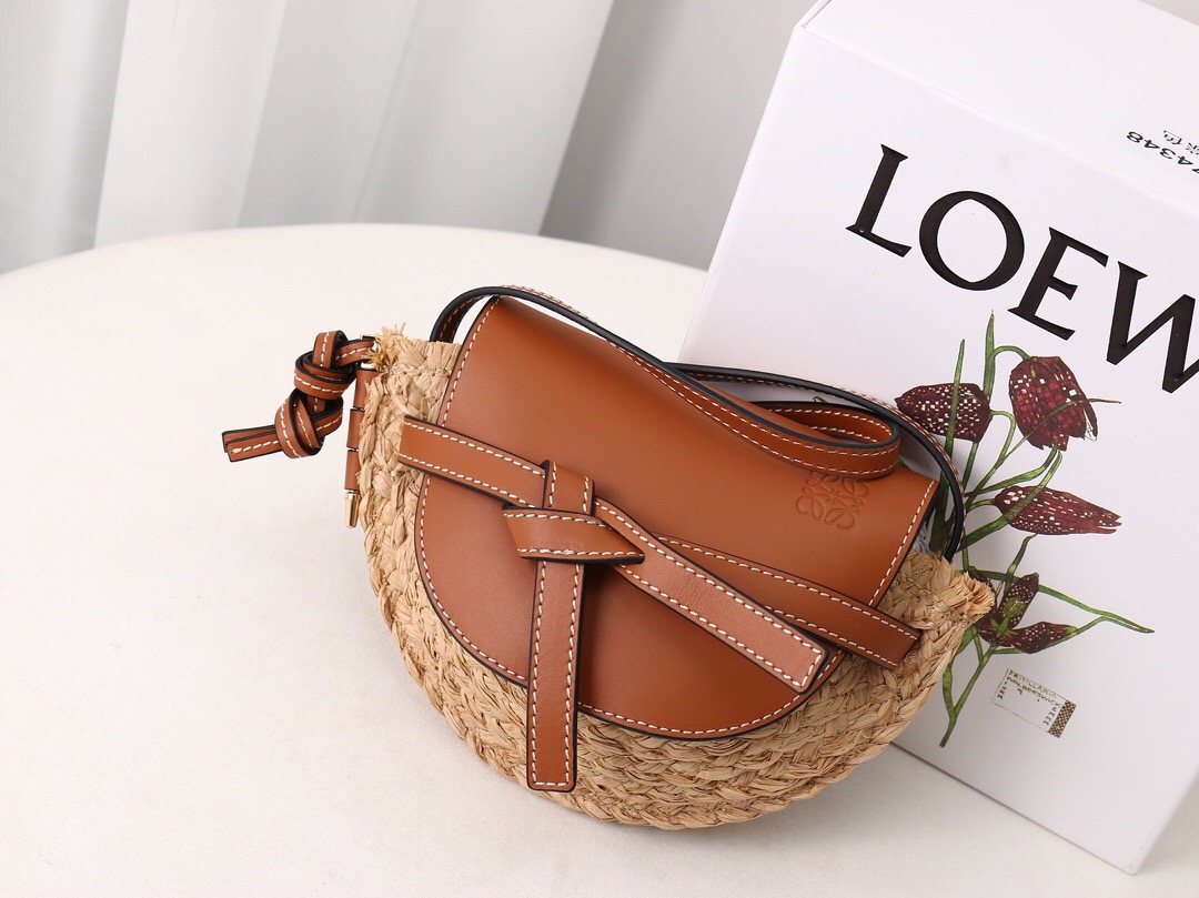 LOEWE Gate Mini Raffia Crossbody Bag. Original Quality Bag. Authentic Soft Calfskin and Woven Raffia. LOEWE Sales Box and Dust Bag. Booklet, Authenticity Card, Payment Slip. Finish off your look with this summery woven raffia iteration of Loewe's beloved Gate bag. The mini silhouette features a contrasting flap closure, which has been made from calf leather with an elegant knot detail wrapping over the front. Think of it as the sort of piece that you'll buy now but love forever. | CRIS&COCO | High quality designer bags and authentic luxury