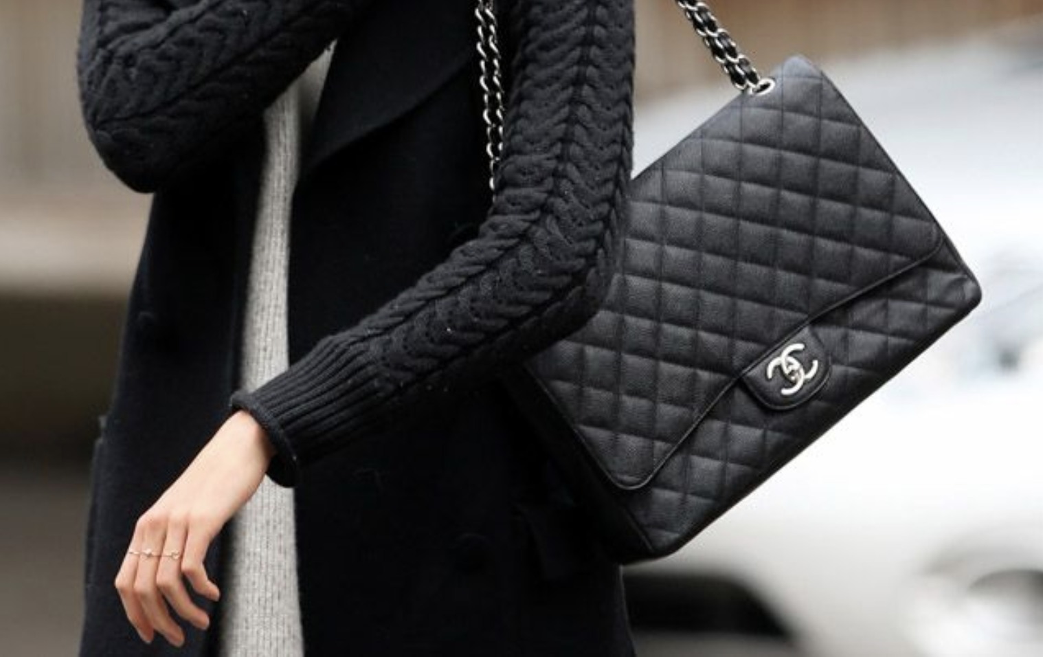 Woman carrying a CHANEL Flap-inspired bag while walking down a city street. A woman wearing a CHANEL Flap-inspired bag, strolling down a city street.