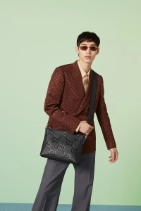 Stylish man walking confidently in a cityscape carrying a sleek luxury messenger bag.
