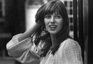 Jane Birkin leaning against a railing in a relaxed outfit with natural makeup