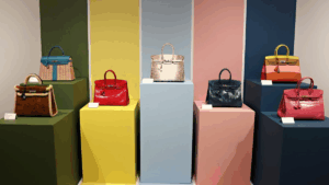 A display of colorful Hermès Birkin handbags on pastel and jewel-toned pedestals in a boutique or exhibition.