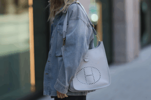 A stylish street look featuring a white leather bag with the iconic "H" logo, paired with a denim jacket.