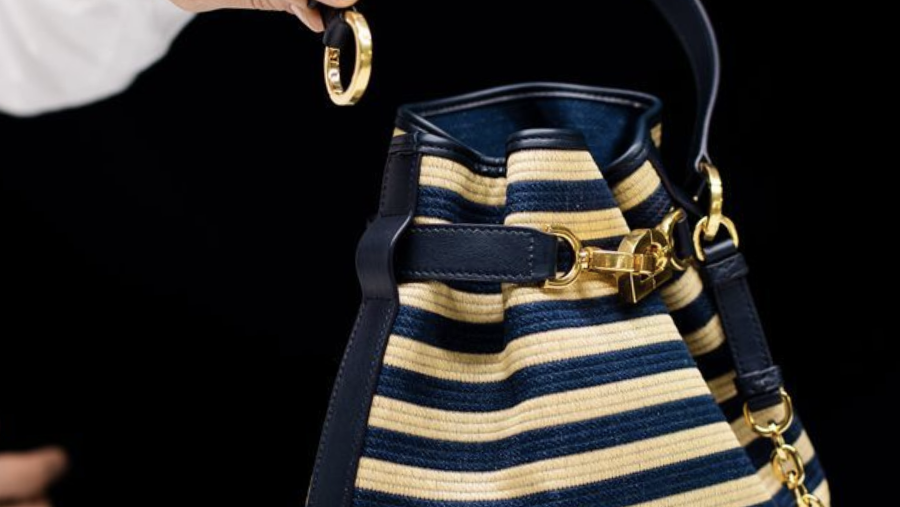 Close-up of a Dior C’est Bag in striped raffia and leather with gold accents, showcasing craftsmanship and texture. Close-up of a Dior C’est Bag in striped raffia and leather with gold accents, showcasing craftsmanship and texture.