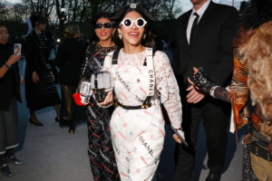 Fashion-forward woman in a white quilted Chanel dress with oversized round sunglasses posing for photos at a gala.