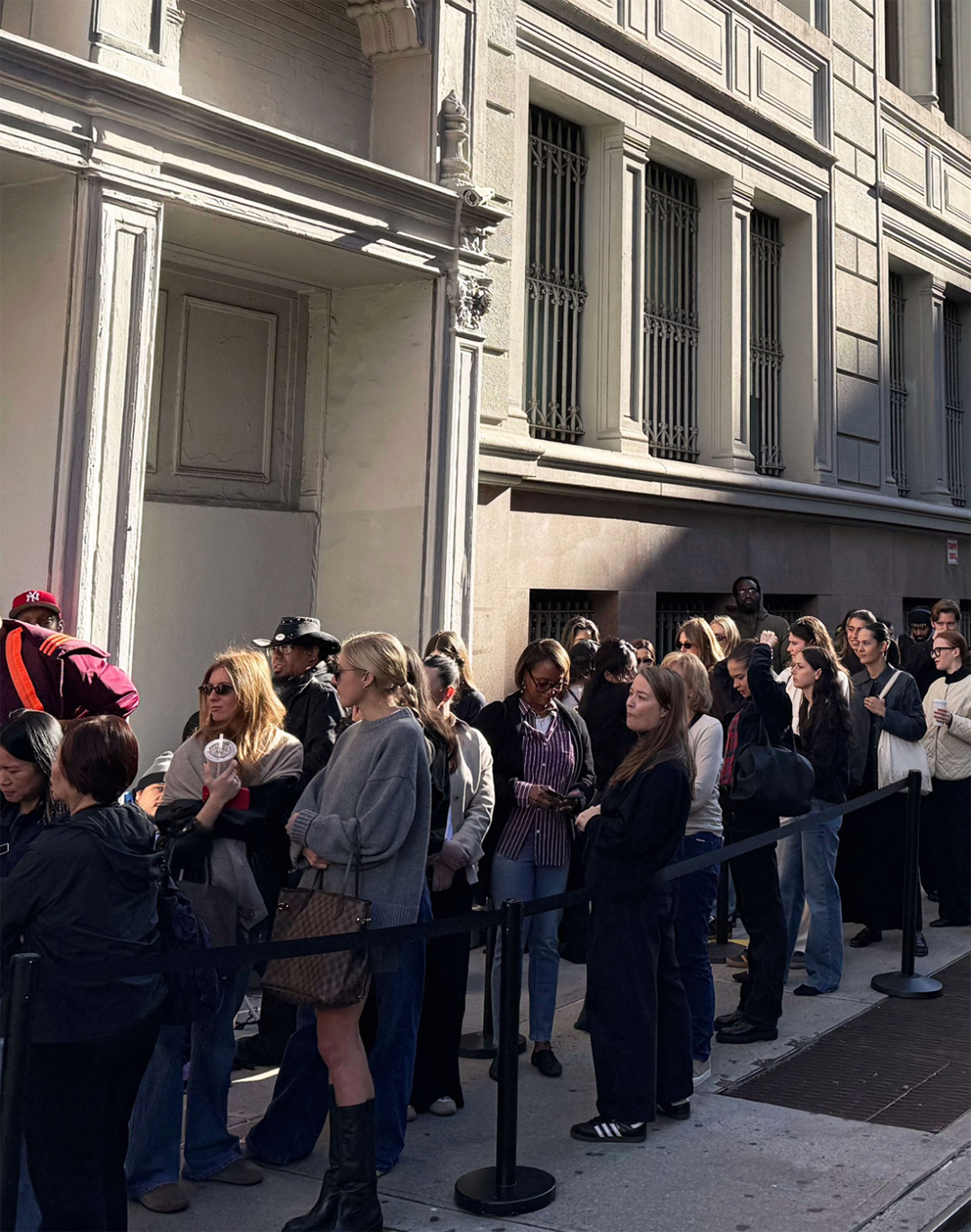 Shoppers waiting in line outside a designer sample sale in Manhattan, New York City, seeking discounted luxury fashion, accessories, and handbags.